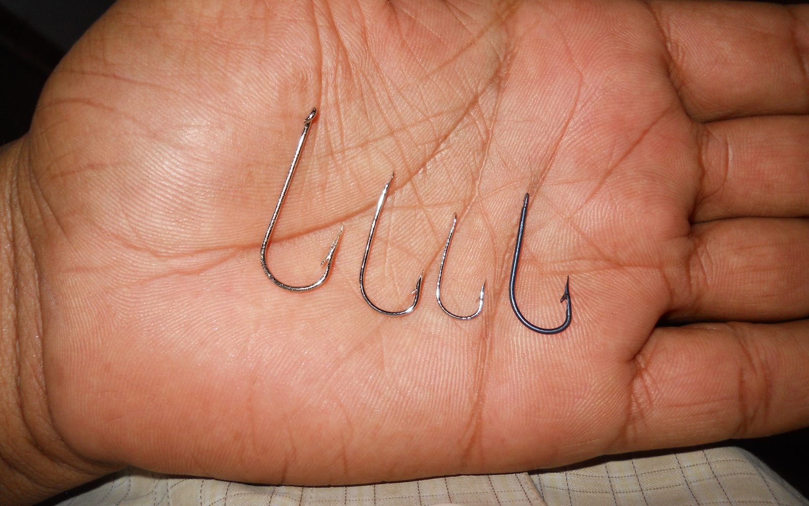Four fishing hooks of different sizes lined up on an open palm
