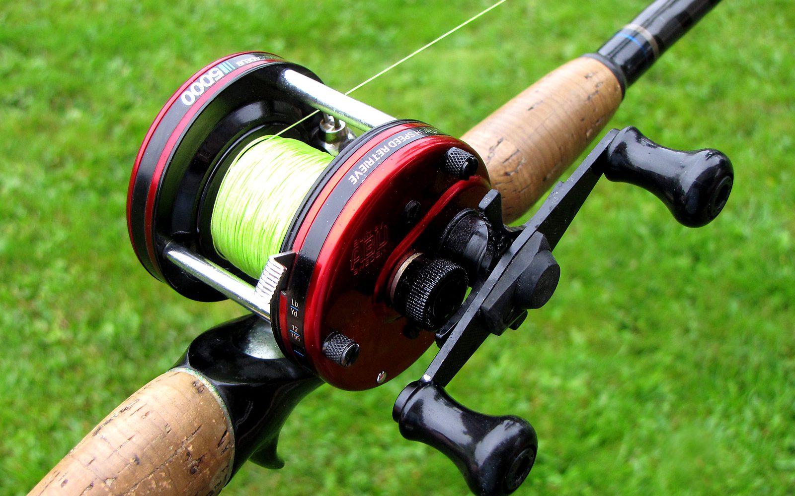 Baitcasting reel mounted on top of a rod with green line on the spool and a thumb-side spool tension knob