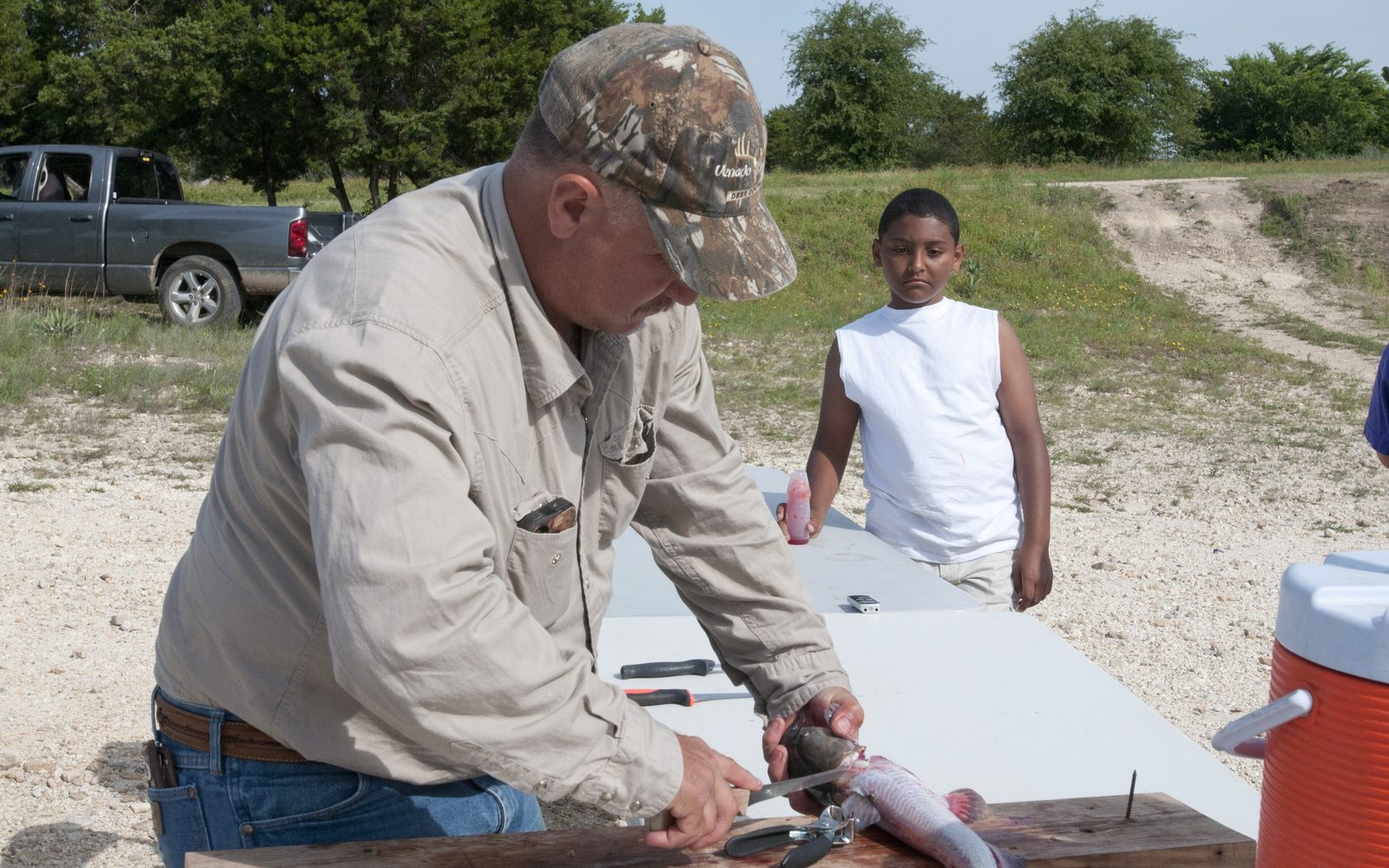 Volunteer instructor cleaning a catfish on a board with pliers and knife at a family fishing clinic