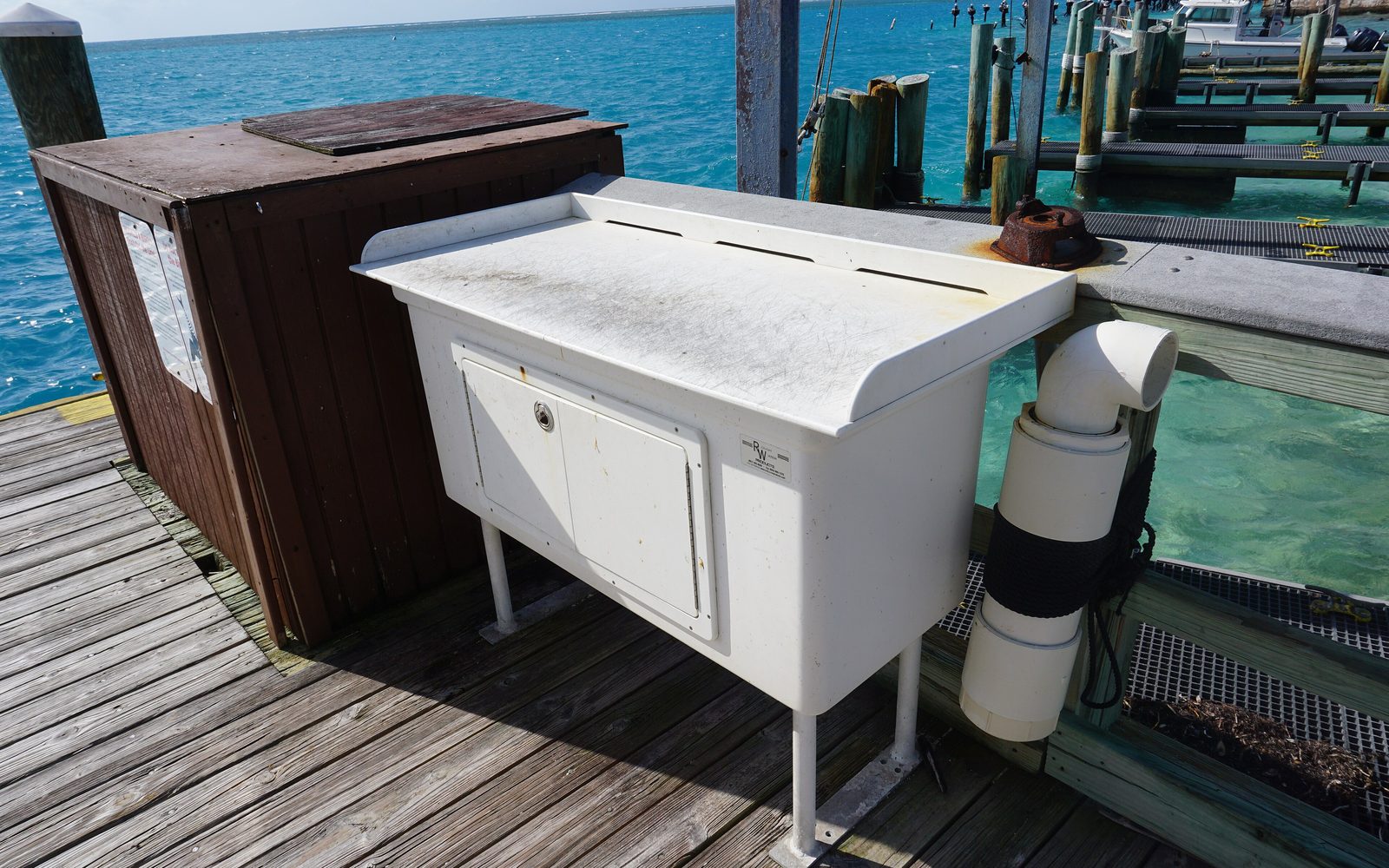 Fish cleaning station on a dock with a cutting table, drain pipe and clear water behind it