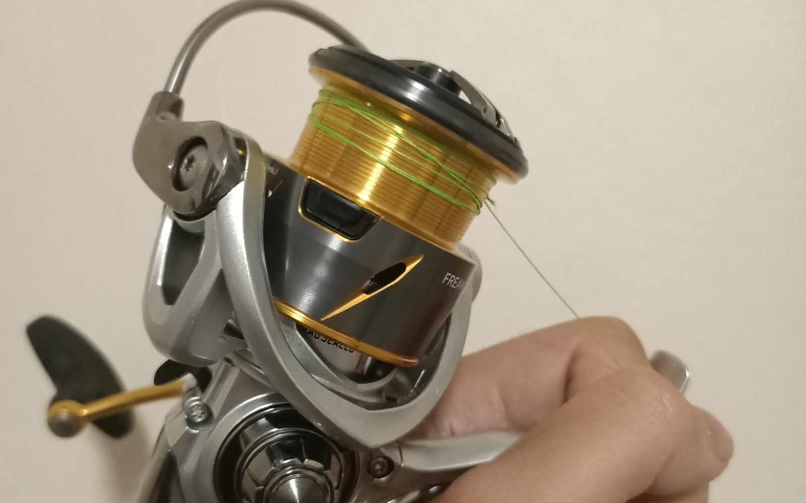 Spinning reel with the bail arm open and fishing line tied to the spool, held in one hand
