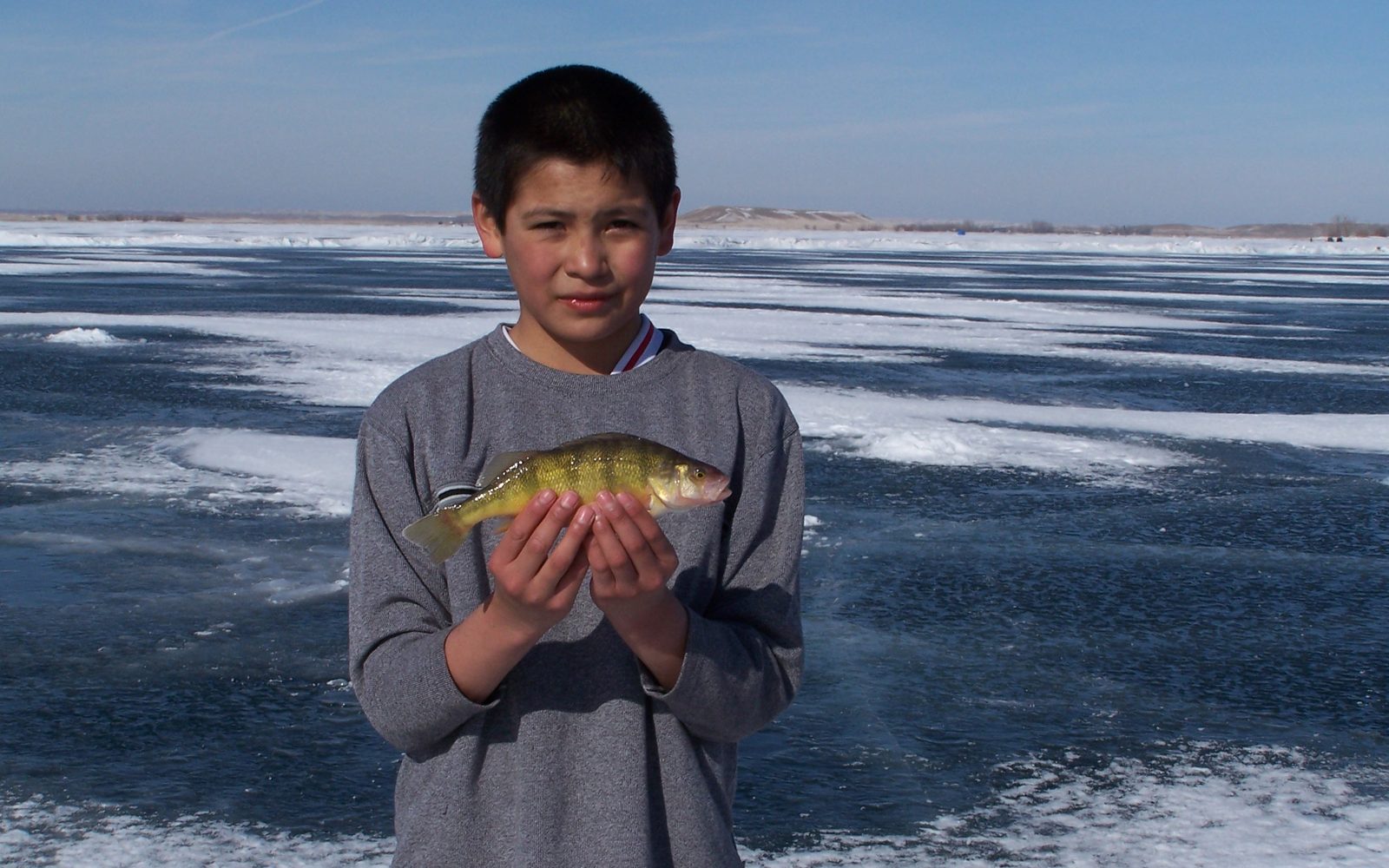 Boy holding a yellow perch in both hands on a frozen lake