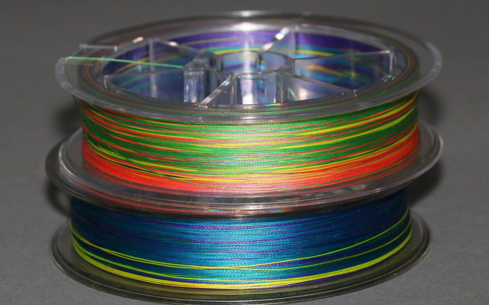 Two plastic spools of multi-colored braided fishing line stacked on a gray surface