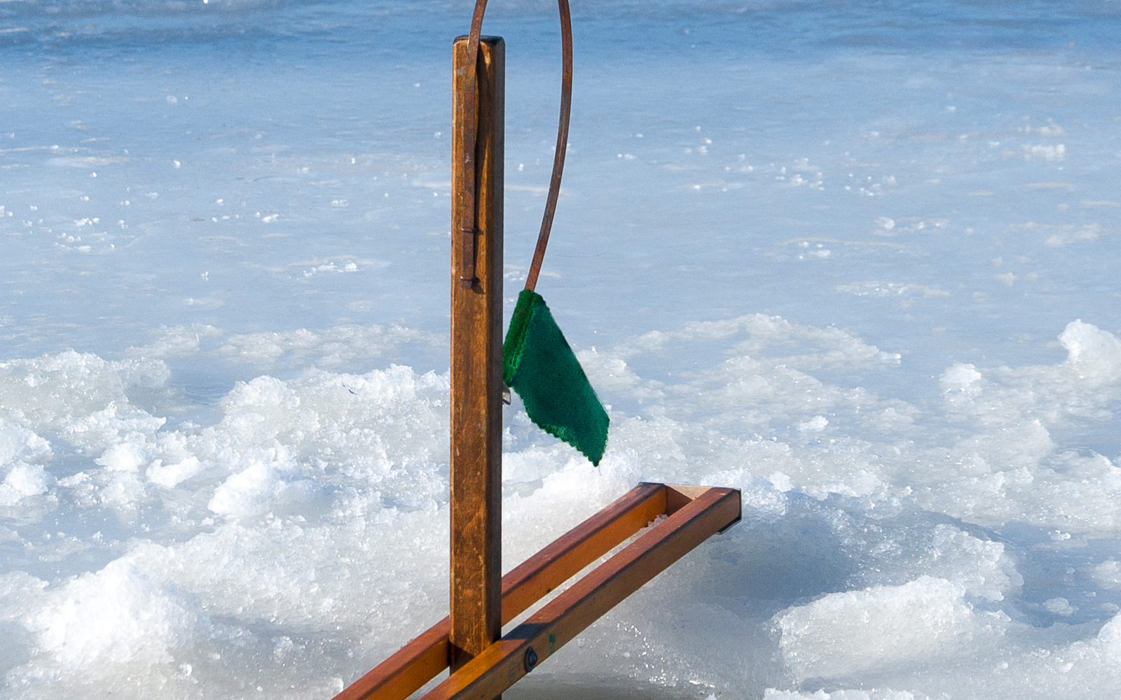 Wooden ice fishing tip-up with a green flag standing over a hole in the ice
